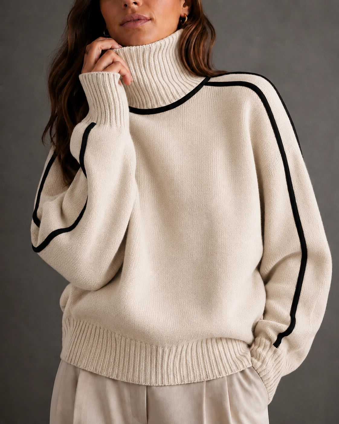 woman wearing a cream-colored ribbed knit turtleneck sweater with black contrast piping along the shoulders and sleeves