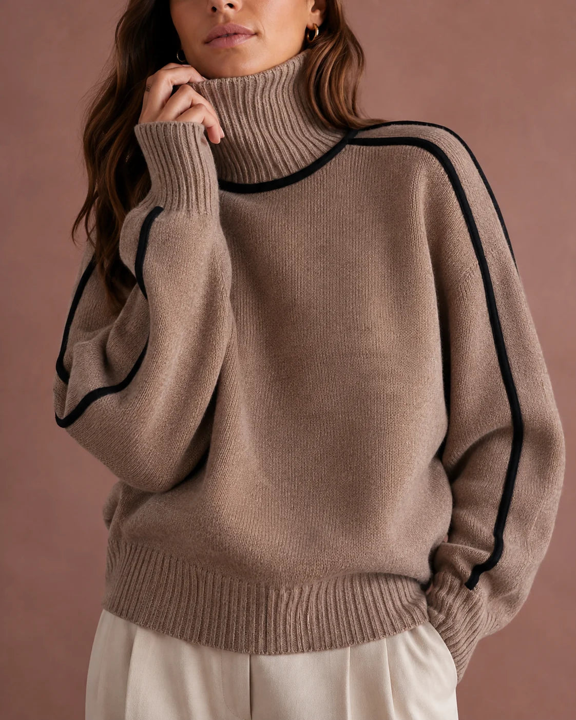 woman wearing a taupe knit turtleneck sweater with black contrast piping along the shoulders and sleeves